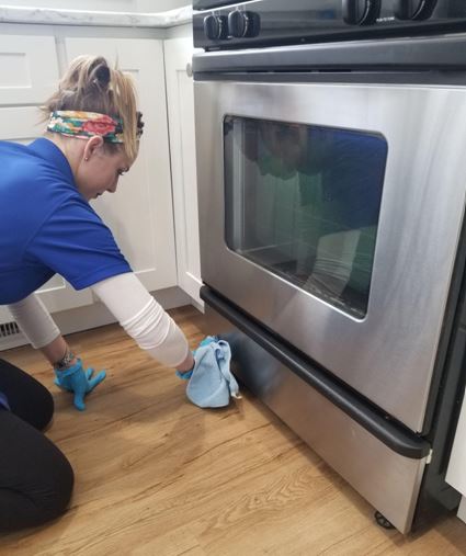 Professional cleaner running rag underneath oven